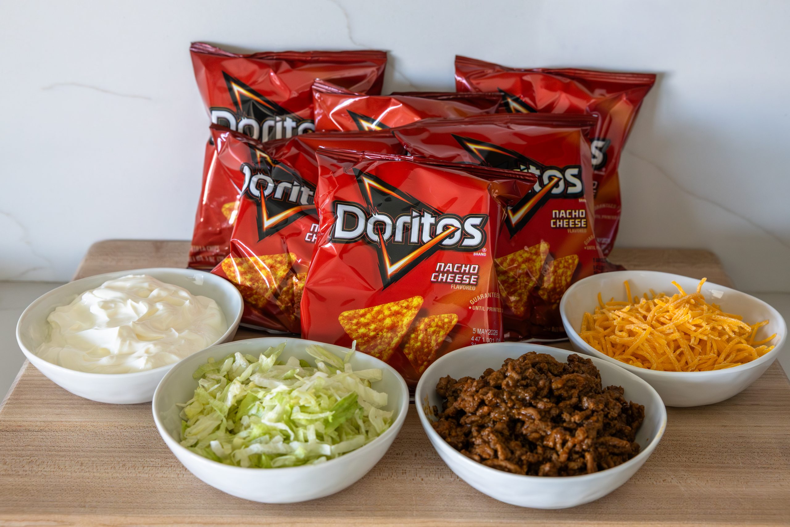 ingredients for walking tacos including ground beef, chips, shredded lettuce, cheese, and sour cream